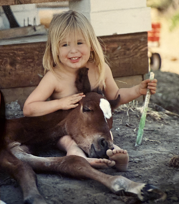 a little girl sitting with a baby horse in the dirt